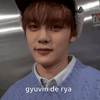 a young man wearing a blue sweater and a hat with the words gyuvin de rya written on the bottom