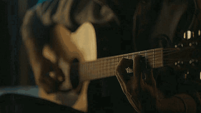 a man is playing a guitar in a dark room in front of a window .