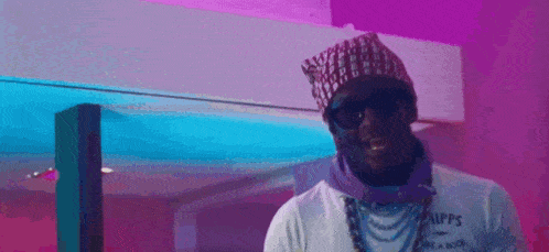 a man wearing a beanie and sunglasses is standing in front of a pink wall