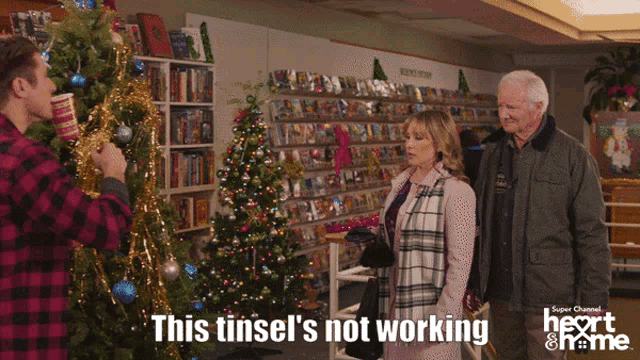 a man decorating a christmas tree with the words " this tinsel 's not working " above him