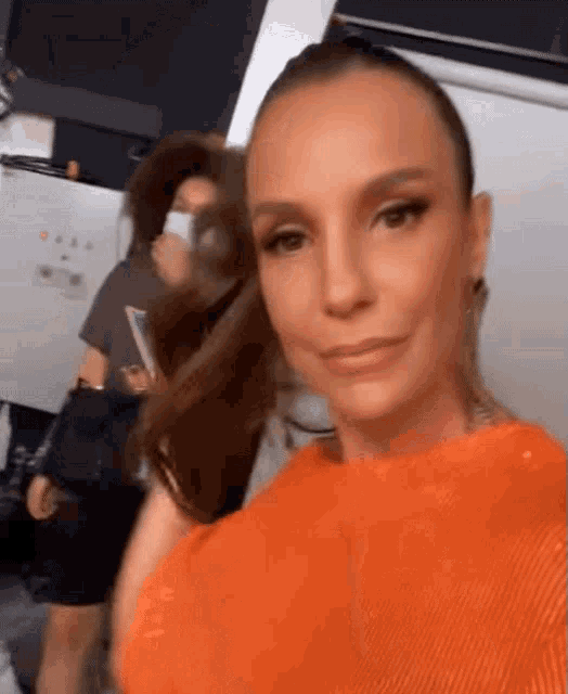 a woman in an orange top is taking a selfie with another woman in a mask .