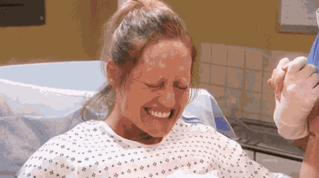 a woman in a hospital gown is crying while holding a baby in her arms .