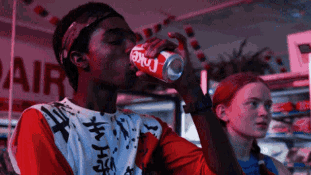 a man is drinking from a can of coke while a woman looks on .