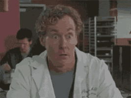 a man in a lab coat is making a surprised face in a kitchen .