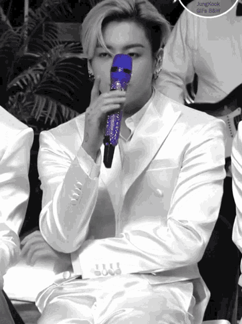 a man in a white suit holds a blue microphone in his mouth