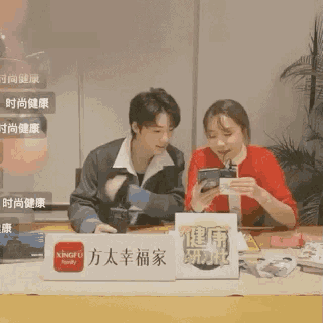 a man and a woman sit at a table looking at their phones