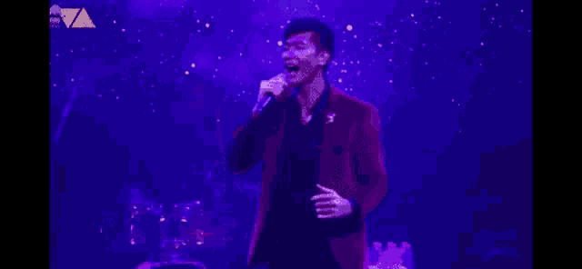 a man is singing into a microphone on a stage in front of a purple background .