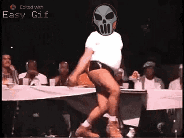a man with a skull on his head is dancing in front of a table with people sitting at it ..