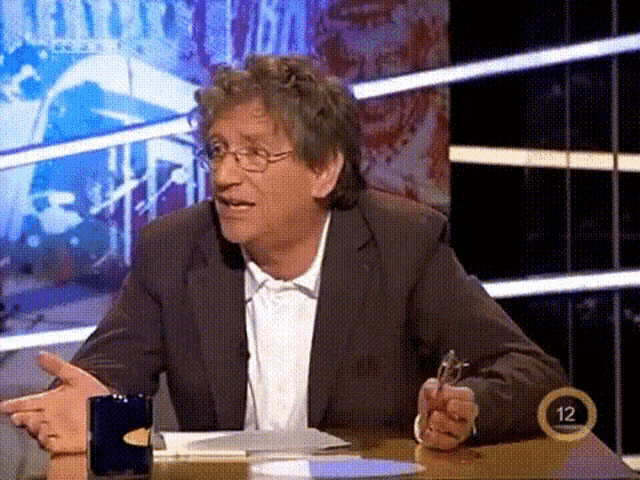 a man in a suit is sitting at a table with the number 12 in the corner