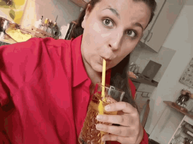 a woman in a red shirt drinks through a straw from a glass