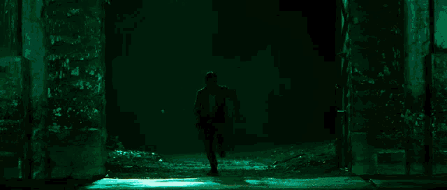 a man is walking through a dark tunnel with green lights behind him