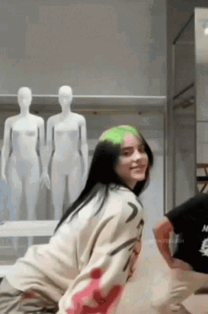 billie eilish is dancing in front of a mannequin in a room .