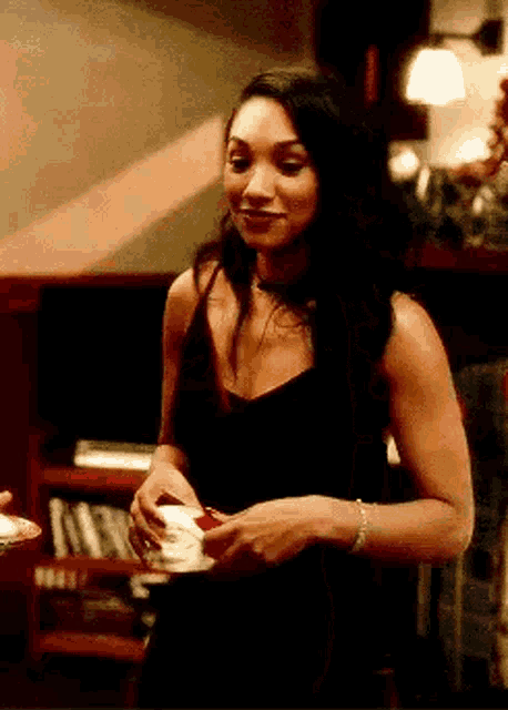 a woman in a black tank top is holding a cup of coffee and smiling .