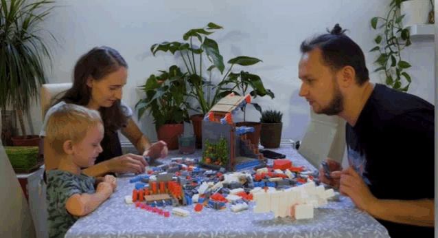 a man and a woman sit at a table with a child playing with lego