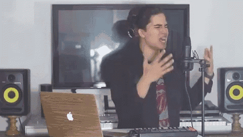 a man singing into a microphone in front of a laptop and speakers