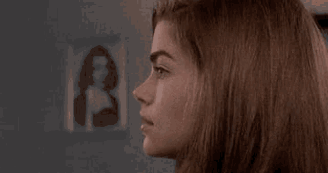 a close up of a woman 's face with a picture of a woman on the wall in the background .