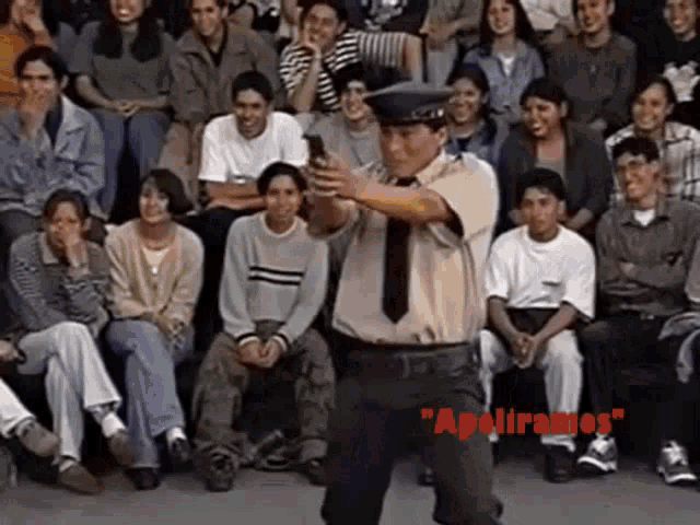 a man in a police uniform is standing in front of a crowd holding a cell phone .