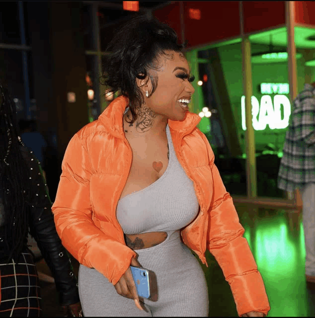 a woman wearing an orange jacket stands in front of a green sign that says bad