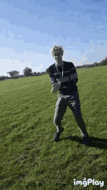 a man in a striped shirt is standing in a grassy field with a blue sky in the background ..