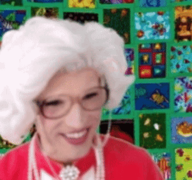 a woman wearing glasses and a white wig is smiling in front of a green wall