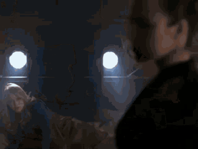 a man and a woman are standing in a dark room with a blue light coming out of a window .