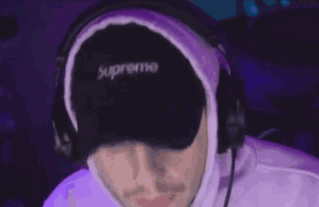 a man wearing headphones and a supreme hat is sitting in front of a computer .