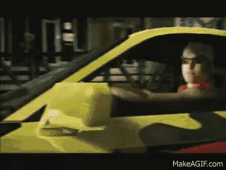 a man in a red shirt is driving a yellow car on makeagif.com
