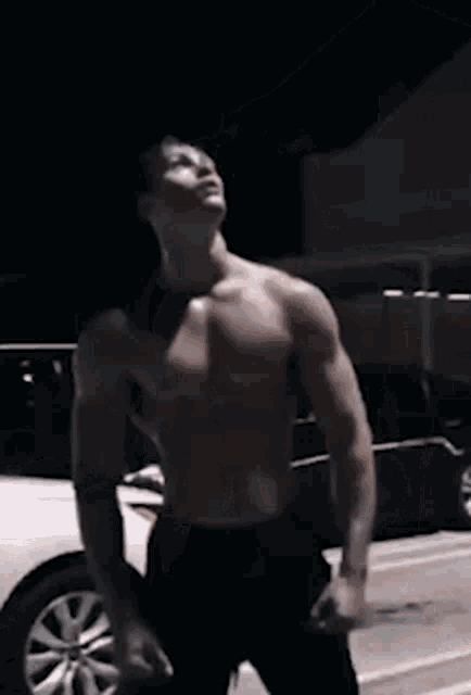 a shirtless man is standing in a parking lot in front of a car .