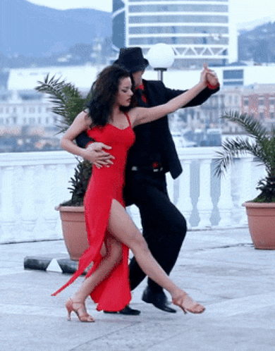 a woman in a red dress is dancing with a man in a black suit and hat