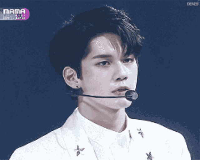 a young man wearing a white suit and a microphone stands in front of a screen that says mama