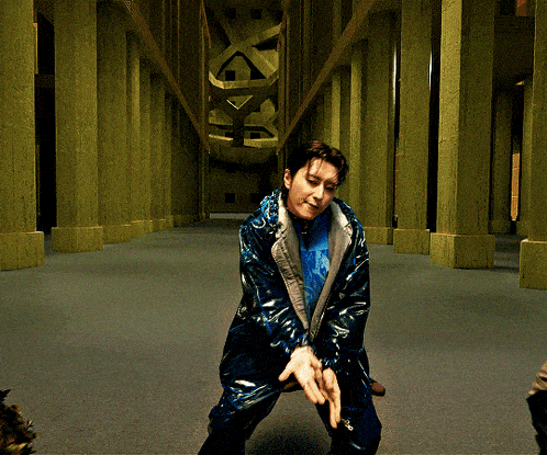 a man in a blue jacket stands in a hallway with columns