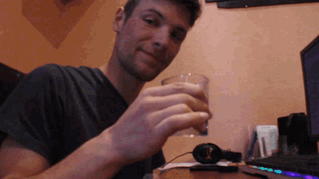 a man holds a glass in front of a laptop and headphones