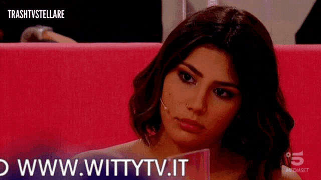 a woman is sitting on a pink couch and the website www.wittytv.it is displayed