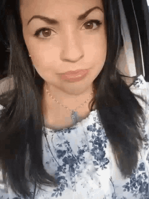 a woman wearing a blue and white floral shirt and a necklace is looking at the camera .