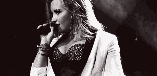a black and white photo of a woman singing into a microphone on stage .