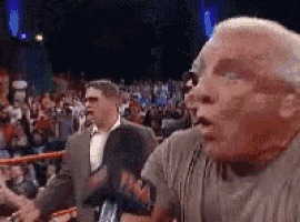 a man in a grey shirt is standing in front of a crowd in a boxing ring