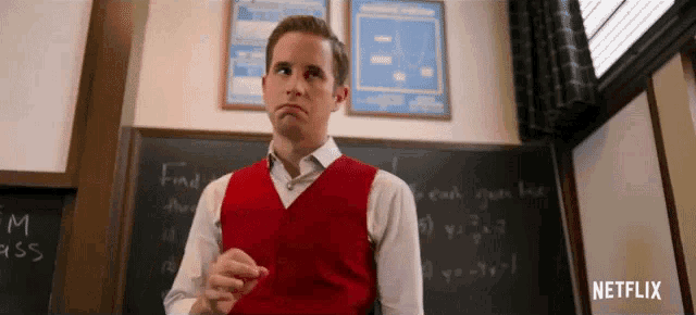 a man in a red vest is standing in front of a blackboard with math problems on it