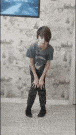 a young boy in a blue shirt and black pants is standing on his knees in a room .