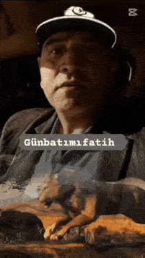 a man wearing a hat is holding a dog with the words günbatimi fatih written on the bottom