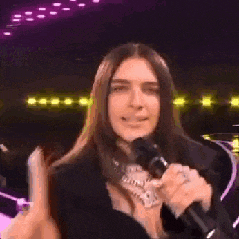 a man with long hair is holding a microphone in his hand and pointing at the camera .