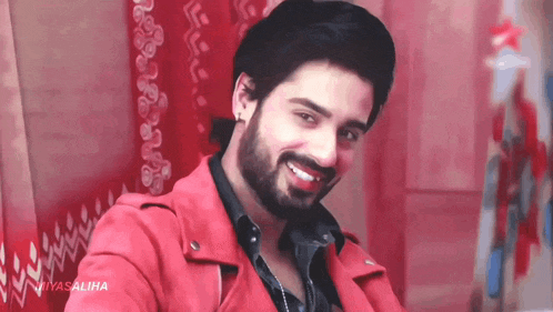 a man with a beard wearing a red jacket is smiling for the camera .