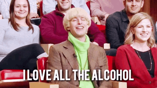 a man in a green sweater is sitting in front of a group of people and says i love all the alcohol