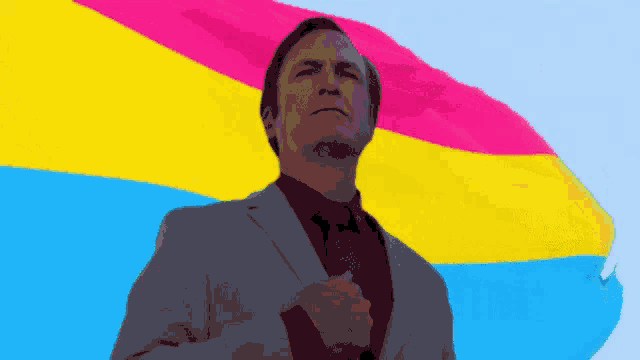 a man in a suit and tie stands in front of a pansexual flag