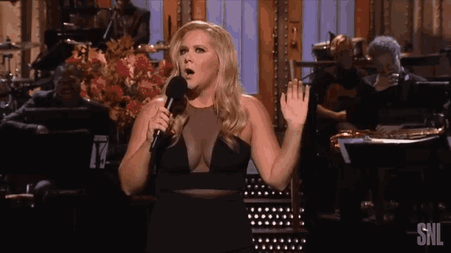 a woman singing into a microphone with the snl logo in the corner