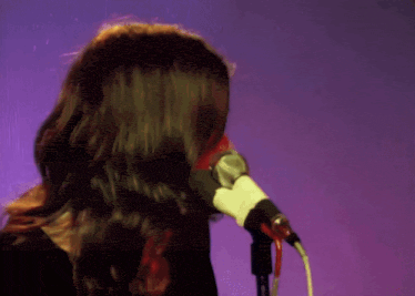 a man singing into a microphone with long hair