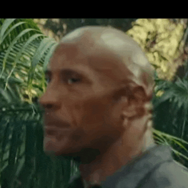 a close up of a man 's face in a jungle with trees in the background .