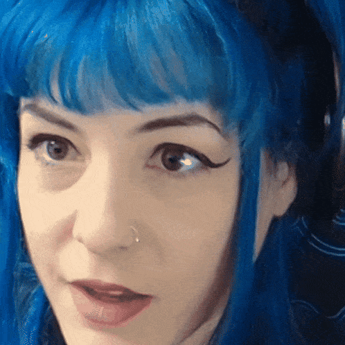 a woman with blue hair and a nose ring looks at the camera