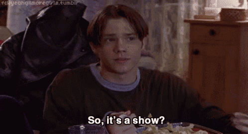a young man is sitting at a table with a plate of food and eating a salad while talking about a show .