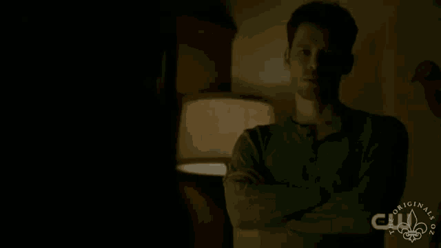 a man stands in a dark room with his arms crossed and a cw logo on the bottom