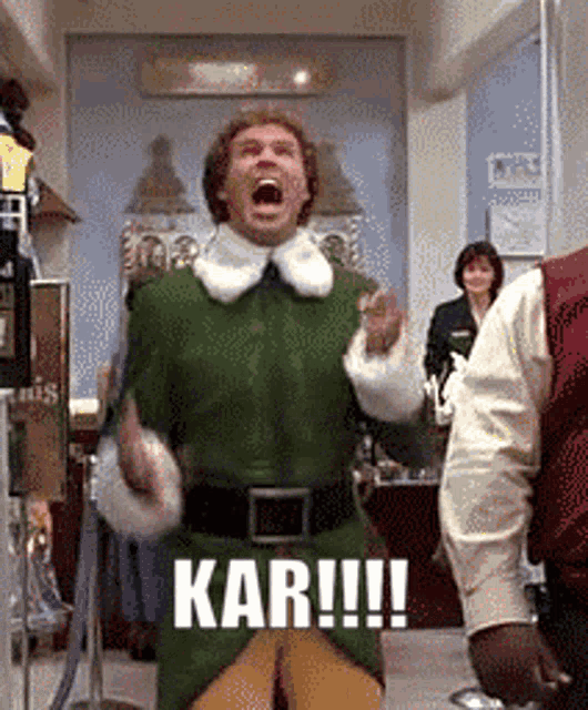 a man in a green elf costume is screaming in a store with the words kar !!! on his chest .
